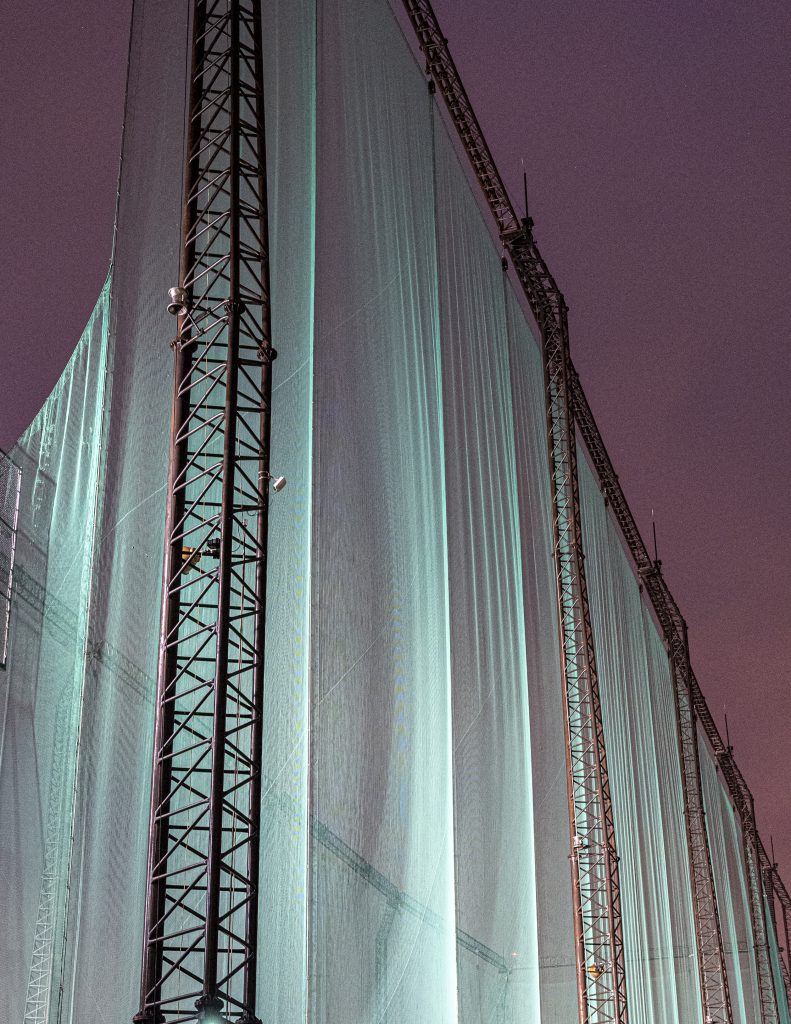Vertical architectural structure with pale illuminated panels and dark metal lines.