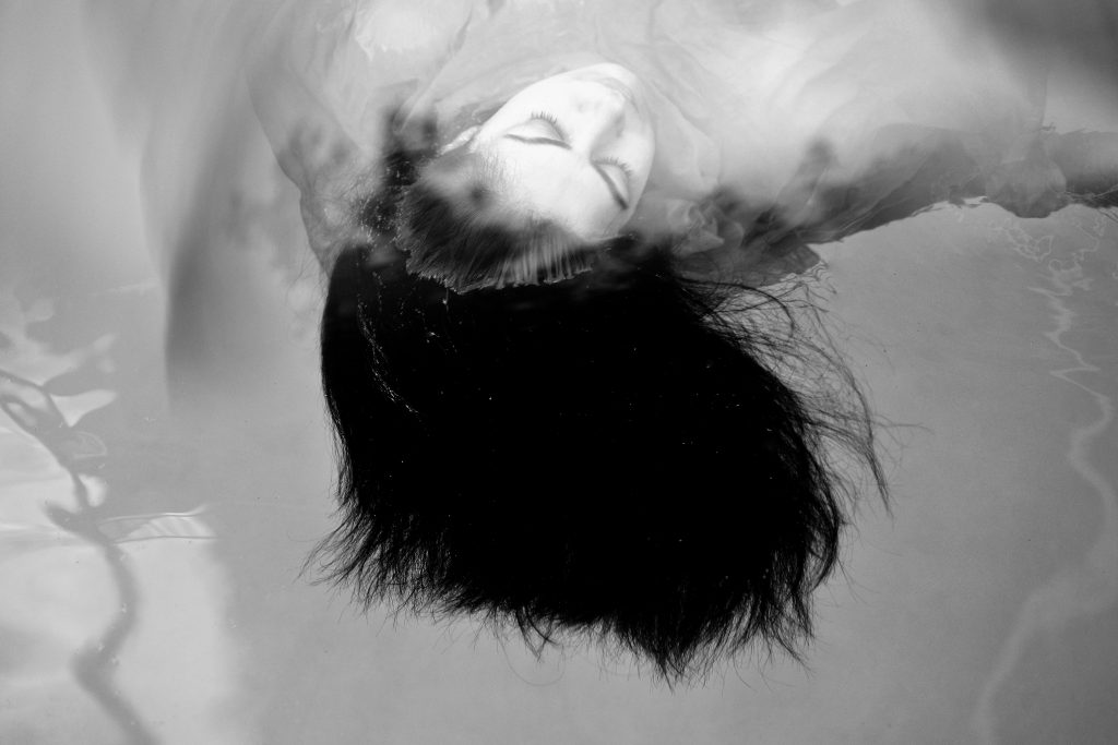 Black-and-white portrait with a figure leaning back and dark hair in motion.