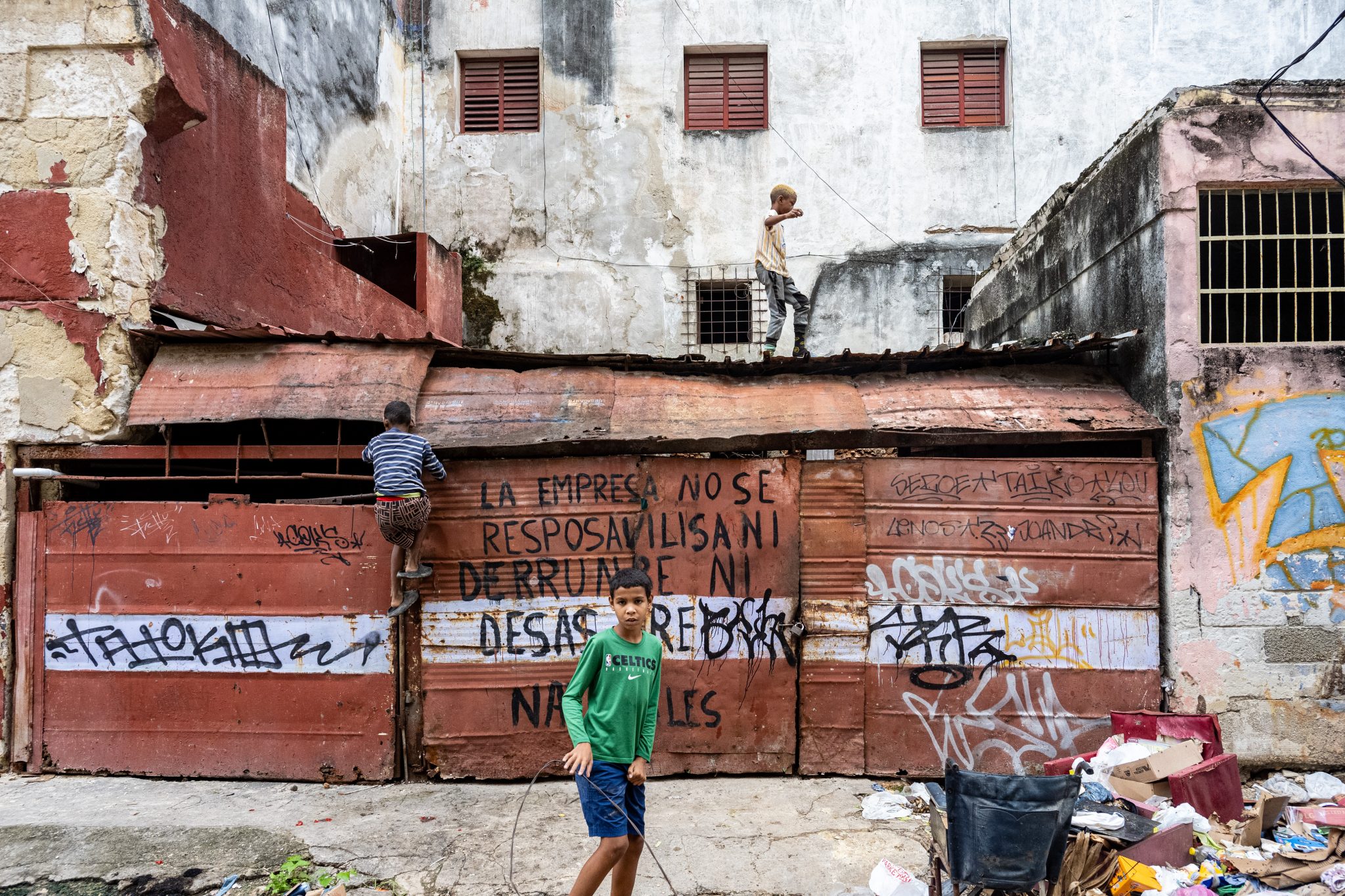 Small figure standing beside a weathered brick wall with graffiti.